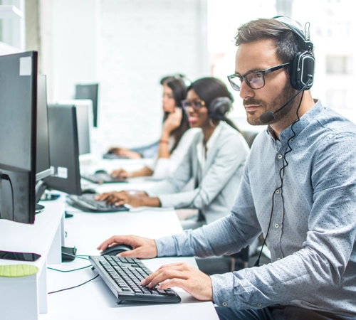 A group of people working on computers while wearing headsets with microphones.