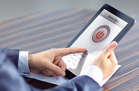 A person is holding a tablet device with both hands, with a large red power button icon displayed in the center of the screen. The text above the icon reads Power Button. The person, dressed in a suit, appears to press the icon with their right index finger, while a wooden surface is visible in the background.