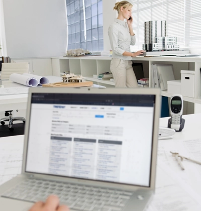 A person on the phone, standing behind a laptop in an office, as seen from afar.